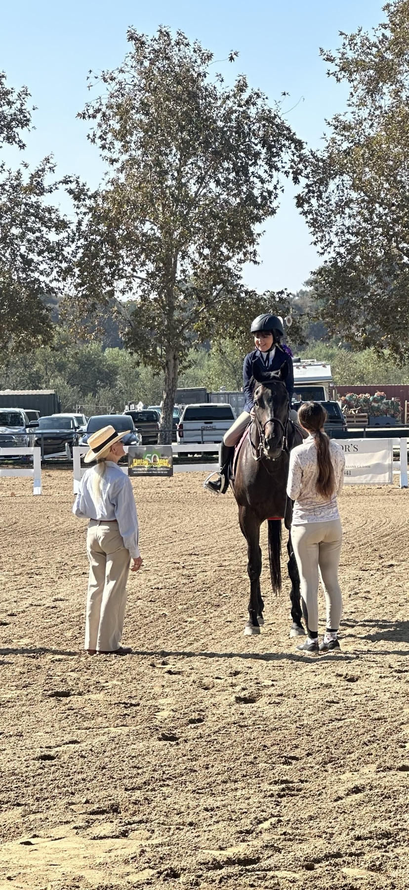 A rider on a dark horse at a show at Hansen Dam Horse Park, with a trainer and a helper at the rail